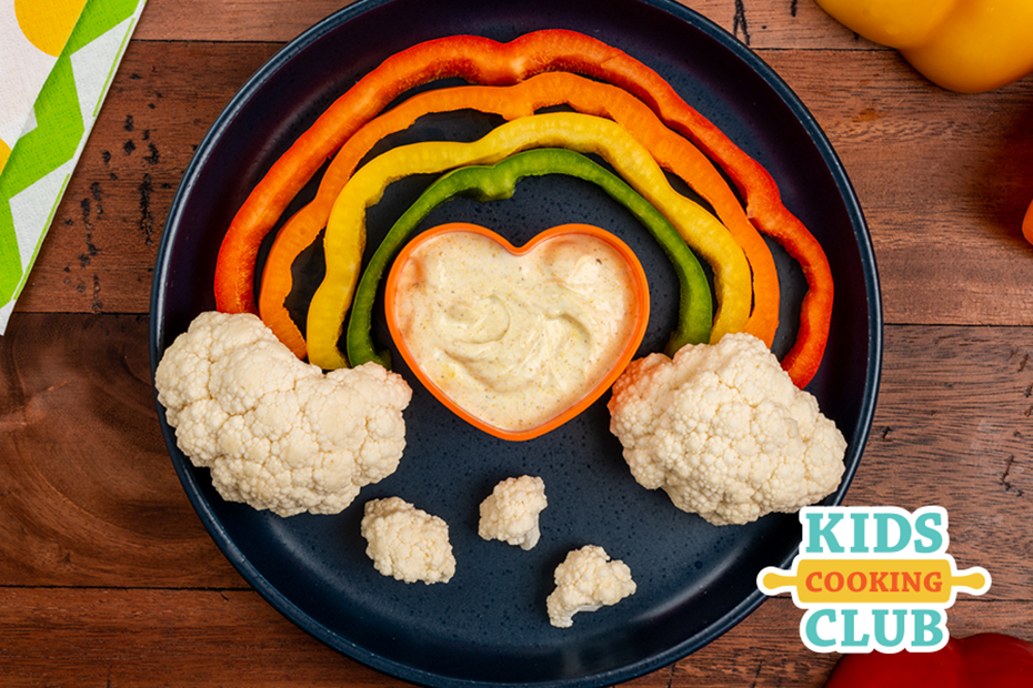 rainbow made with colorful peppers and cauliflower as clouds with a heart-shaped bowl filled with dip- logo Kids Cooking Club