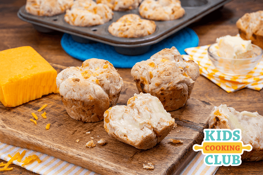 cheesy rolls on a wooden cutting board with a piece of a Cheddar cheese and muffin tin pan.