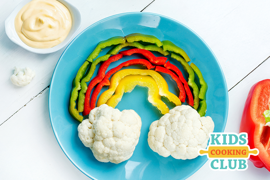 rainbow made with colorful peppers and cauliflower as clouds with a heart-shaped bowl filled with dip