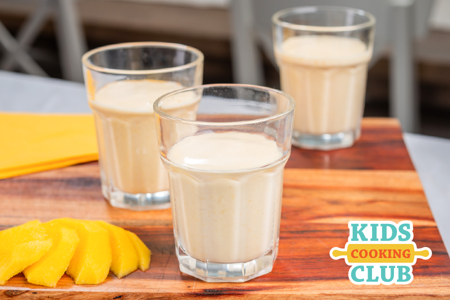 Mango lassi in a glass with a sliced mango beside it
