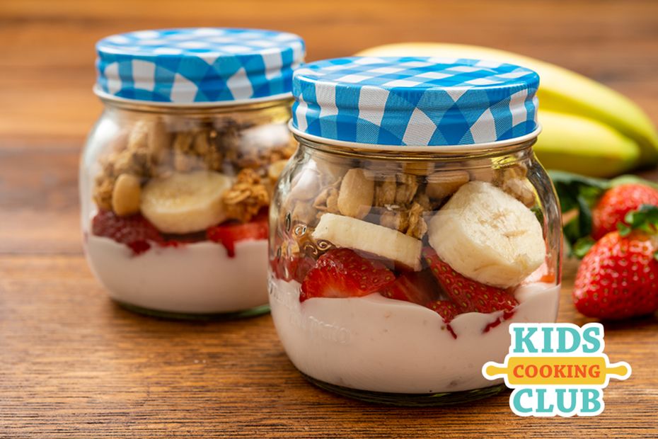 strawberry and banana parfait in a jar on a table. Logo: Kids Cooking Club